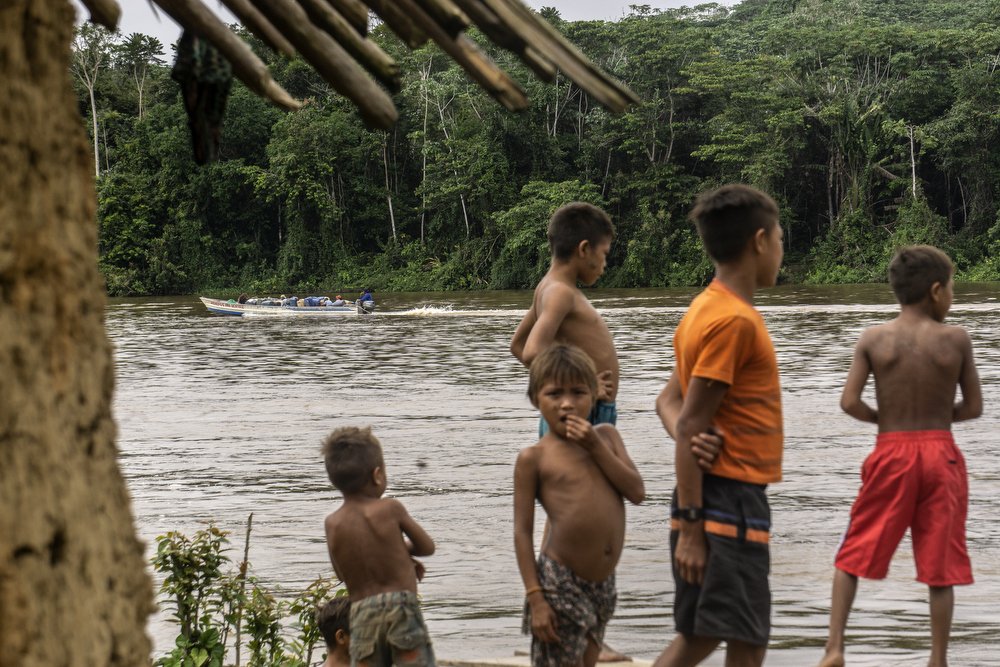 Дети смотрят, как лодка проходит по реке в общине Вайкас