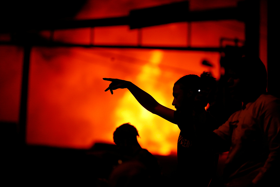A silhouette of a person pointing as protesters gather to watch a liquor store burning