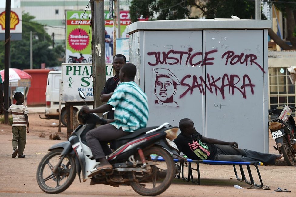 Gente frente a un grafiti que dice "Justicia para Sankara"