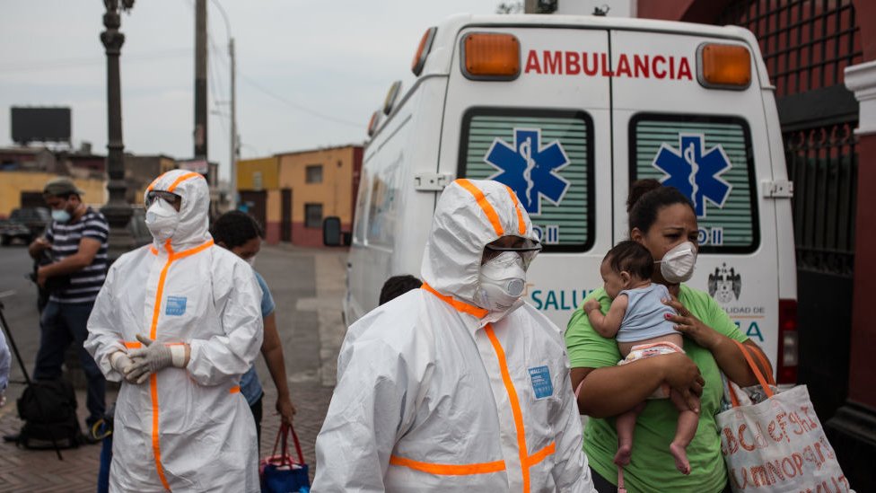 Trabajadores de la salud con equipos de protección personal frente a una ambulancia en Perú