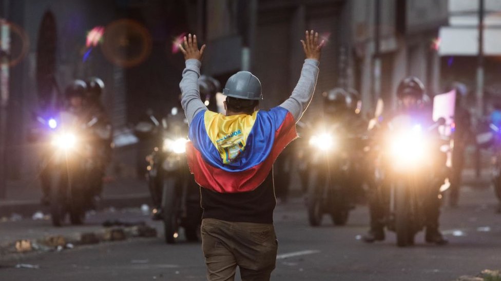 Hombre con una bandera de Ecuador frente a policías