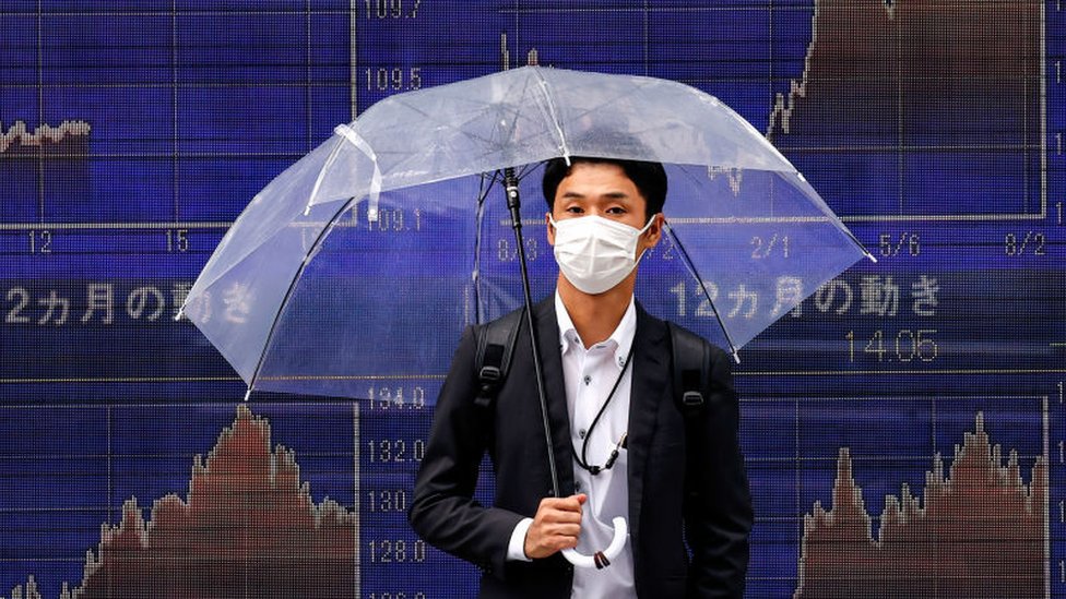 Main holding umbrella in front of stock market charts in Tokyo.