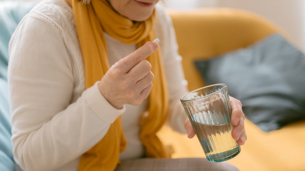Una mujer se toma una pastilla con un vaso de agua