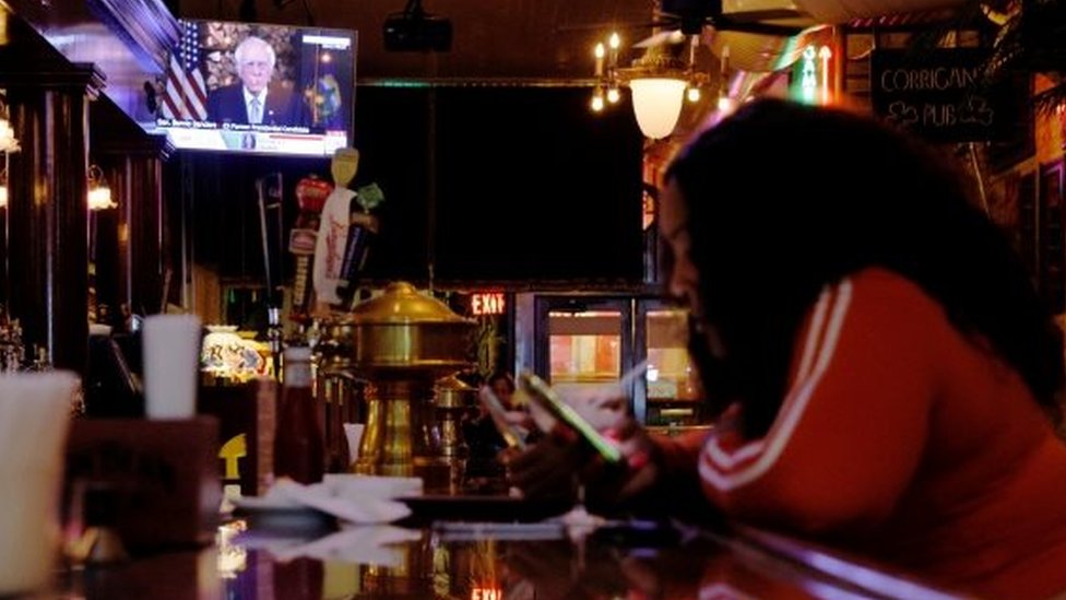 Una mujer en un bar mientras Bernie Sanders está en tv