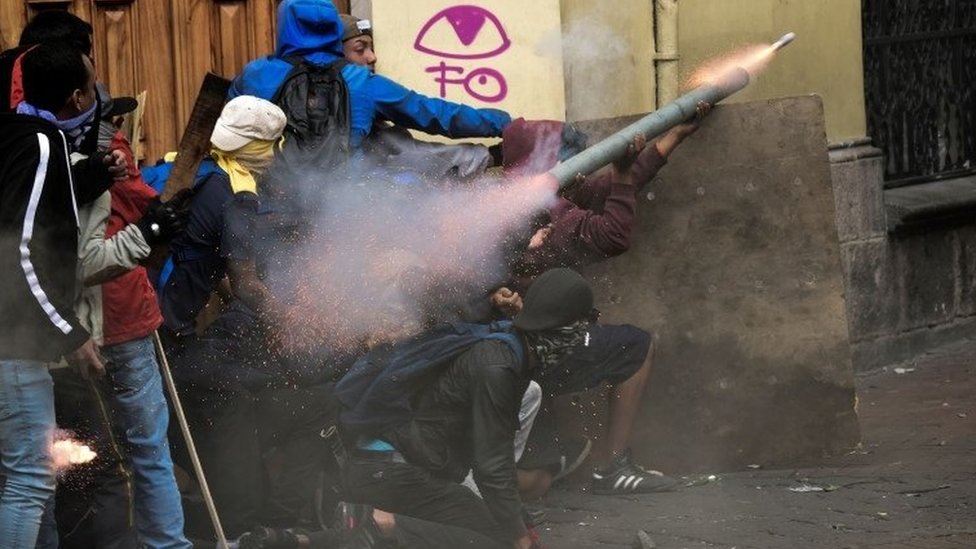 Около семи демонстрантов в капюшонах пытаются выстрелить из самодельного миномета во время столкновений с полицией