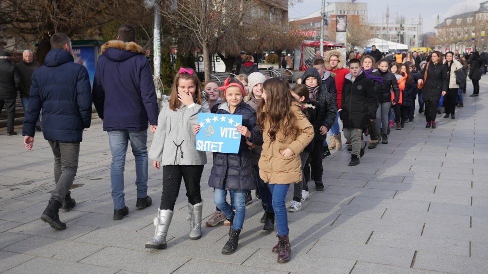 Маленькие дети идут по Приштине с плакатом в честь 10-летия Косово.