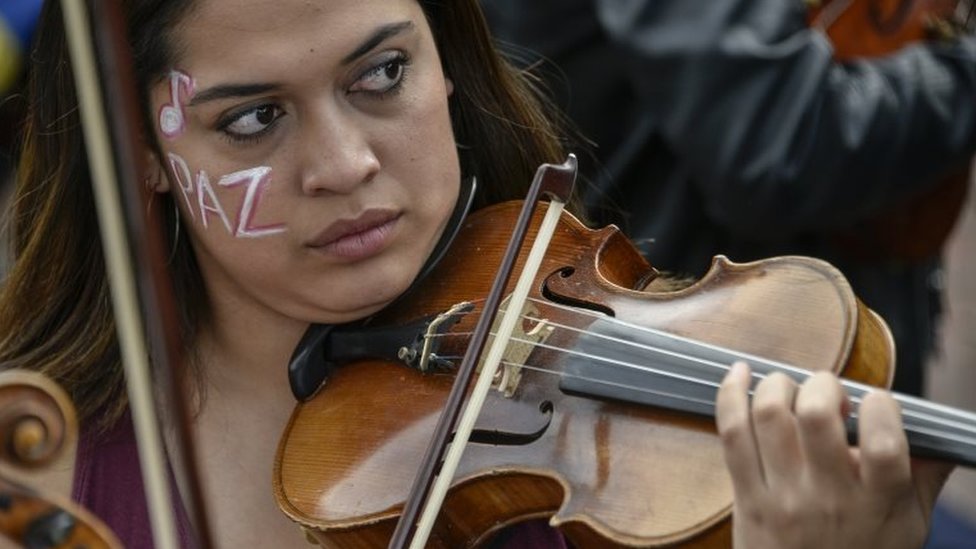 Музыкант консерватории Национального университета Колумбии играет на скрипке с раскрашенным лицом с надписью «мир» во время акций протеста и национальной забастовки против правительства президента Ивана Дуке 27 ноября 2019 года в Боготе, Колумбия
