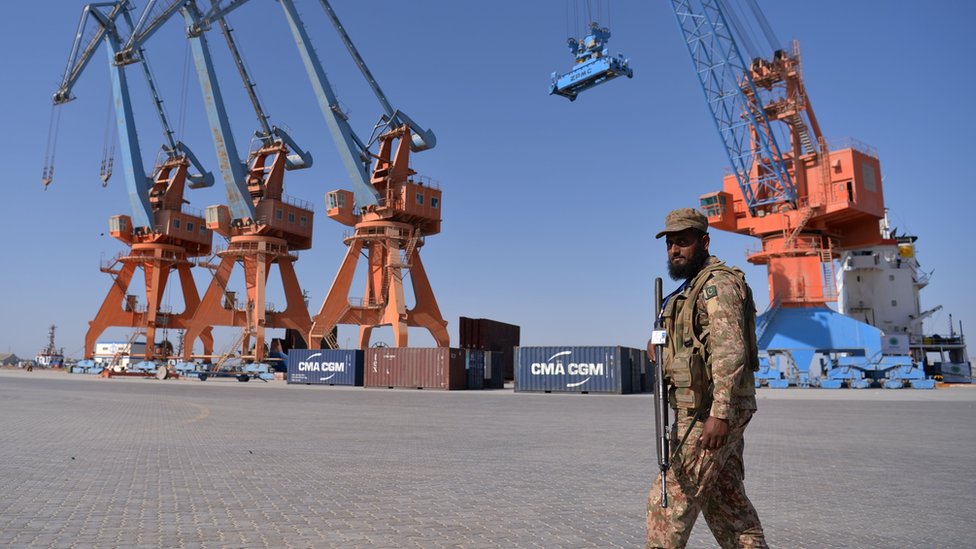 Grúas del puerto con un militar paquistaní armado controlando el área.