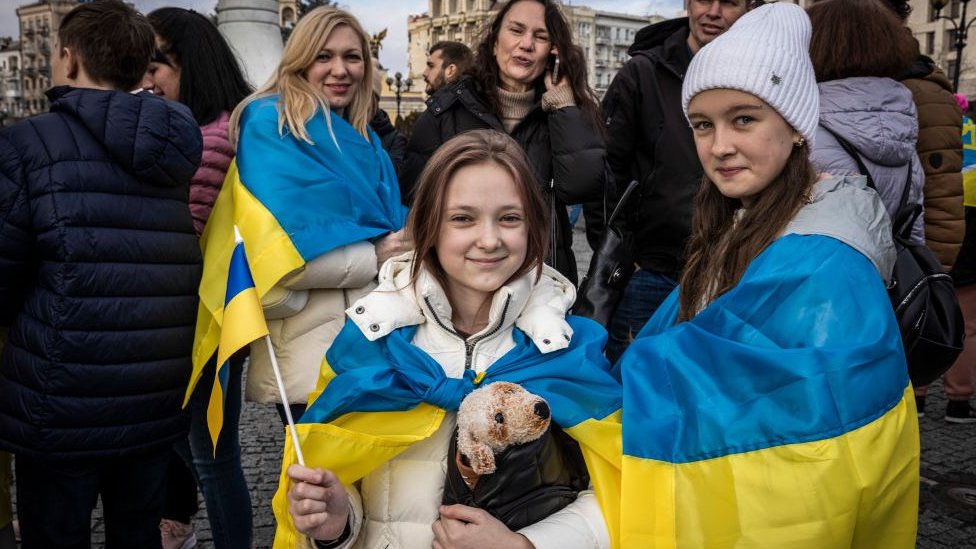 Ucranianas muestran sus banderas y sonríen ante la cámara.