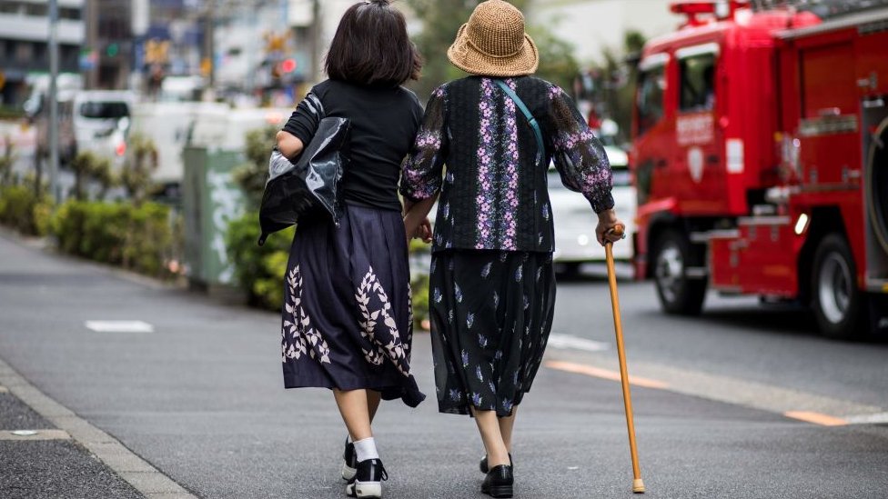 An elderly woman is escorted along a busy road in Tokyo on October 3, 2019.