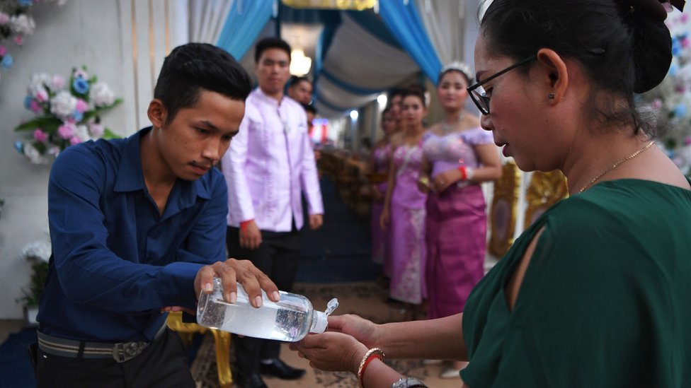 Мужчина делится дезинфицирующим средством для рук с женщиной на свадебной службе в Камбодже