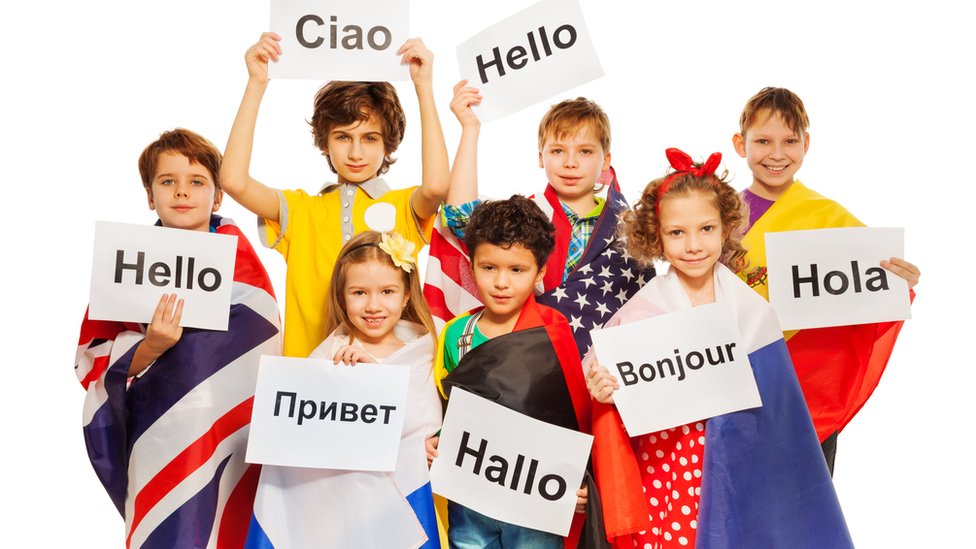 Grupo de niños con disntintas banderasy saludos en distintos idiomas.