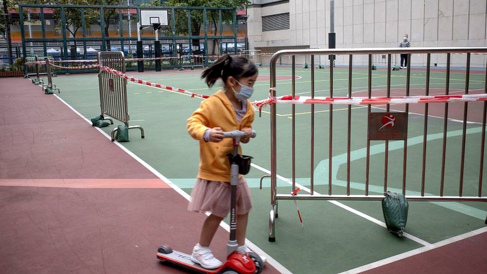 A young girl uses her scooter around a roped-off basketball court, closed due to Covid-19