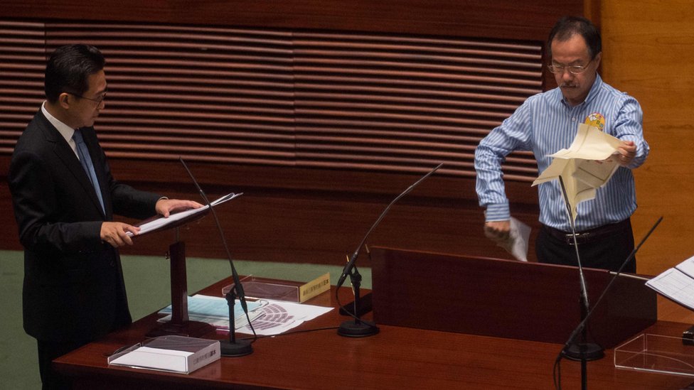 Новоизбранный депутат Фернандо Чунг (справа) разрывает насмешку над «постановлением 831», когда собирается принять присягу Законодательного совета |