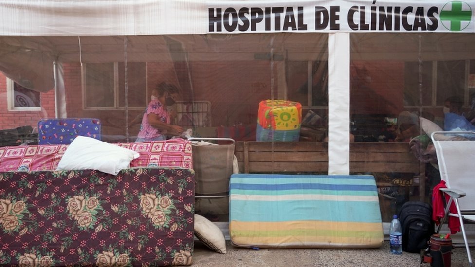 Colchões e malas em frente a fachada que diz: Hospital de Clínicas