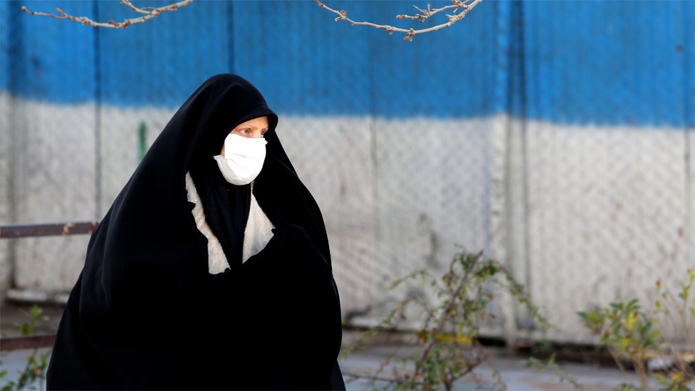 A woman wearing a face mask walks down a street in Tehran (2 March 2020)
