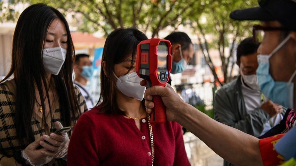 A worker wearing a face mask checks passengers body temperatures and a health code on their phones before they take a taxi after arriving at Hankou railway station in Wuhan, Hubei Province on May 12, 2020.