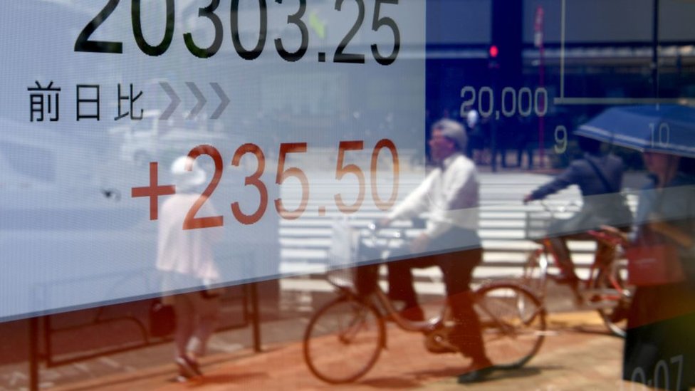 El bajo desempleo no ha generado un aumento significativo de los salarios. Pedestrians are reflected in the window of a securities company displaying the numbers on the Tokyo Stock Exchange along a street in Tokyo
