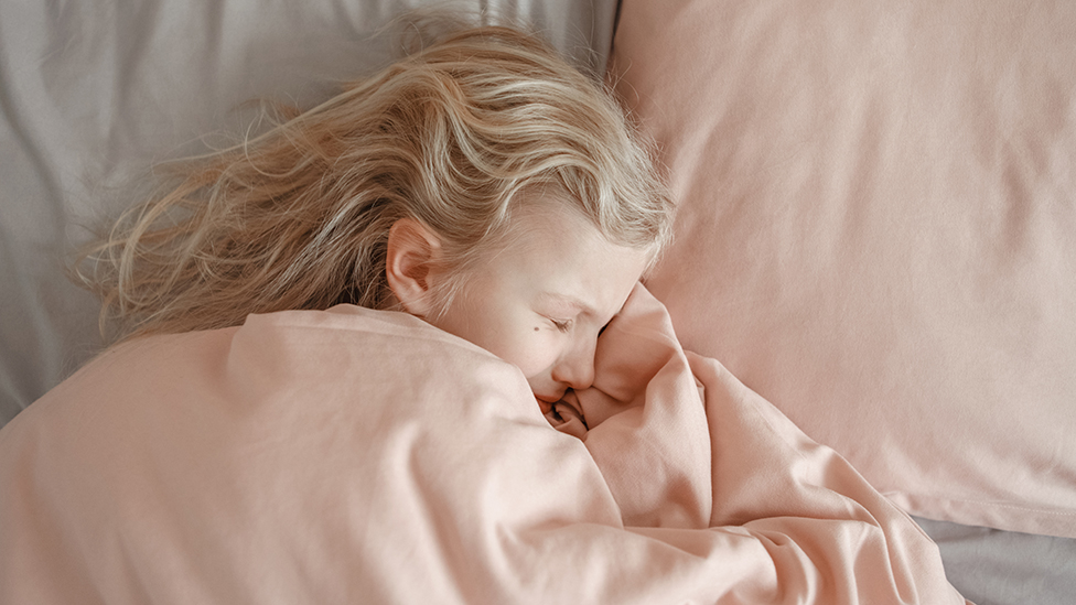 Una niña dormida con cara dolorida.