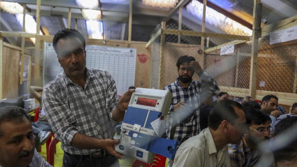 在印控克什米爾夏季首府斯利那加，一名選舉官員向一名監票員展示電子投票機。