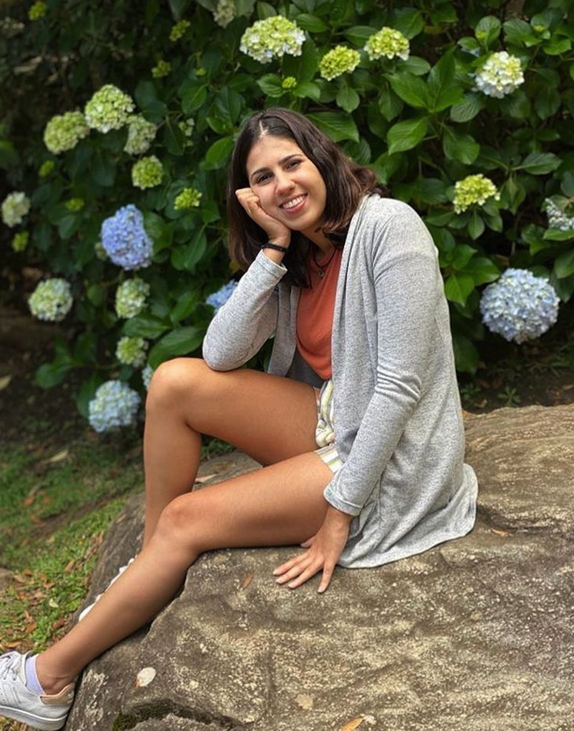 Sorridente, Larissa posa para foto sentada em meio à natureza