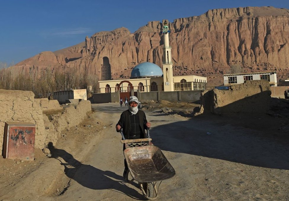A Hazara man pushes a wheelbarrow along a road near the site of the Buddhas of Bamiyan statues