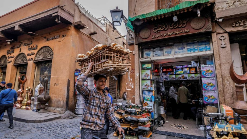 عامل توصيل يوازن رغيف خبز على رأسه وهو يركب دراجة في أحد شوارع الأحياء القديمة في القاهرة.