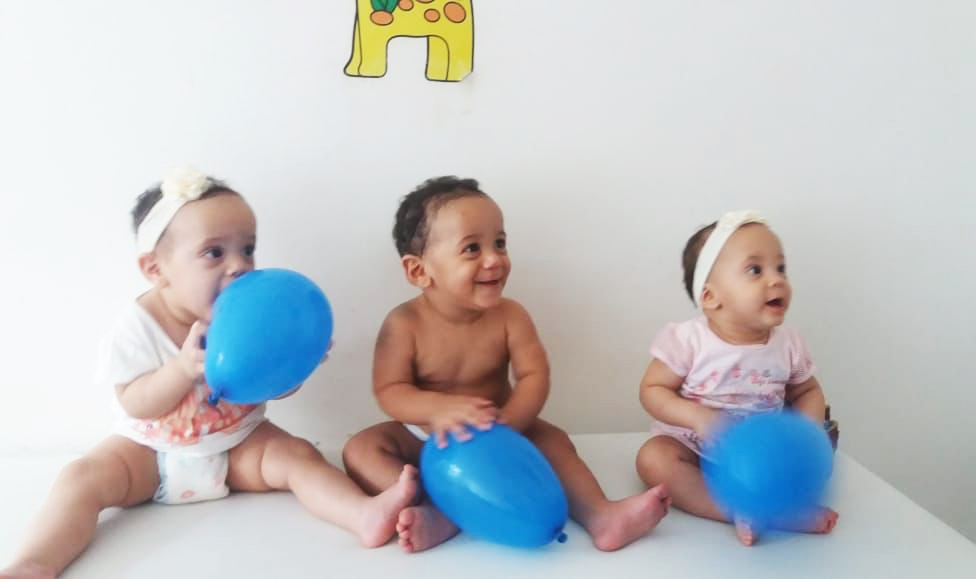 Eloá, Miguel e Helena, os trigêmeos filhos de Glauciele, com cinco meses de idade, sentados segurando bexigas azuis