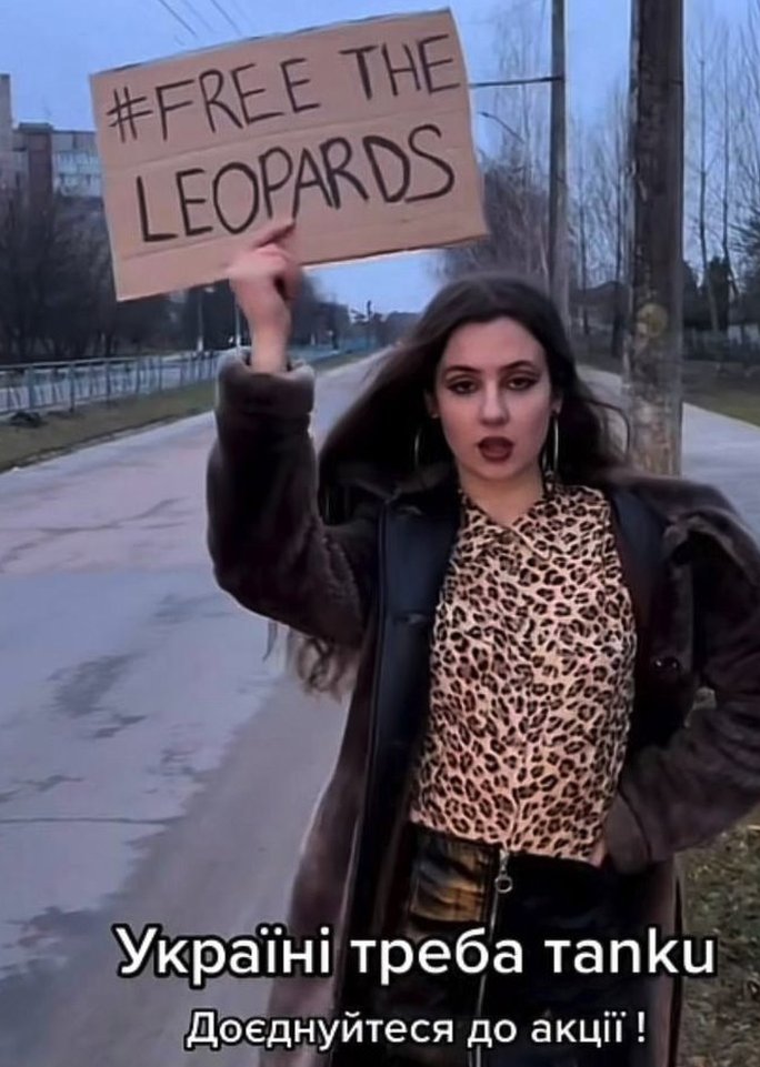 A woman wearing a leopard skin top holds up a sign saying '#Free the leopards'