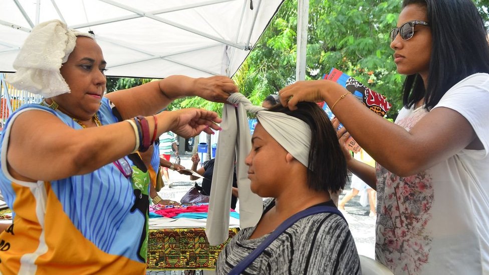 Vendedoras ajudando mulher a vestir turbante