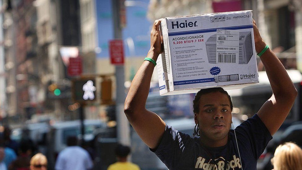 Un hombre carga sobre su cabeza una unidad de aire acondicionado en una calle en Nueva York