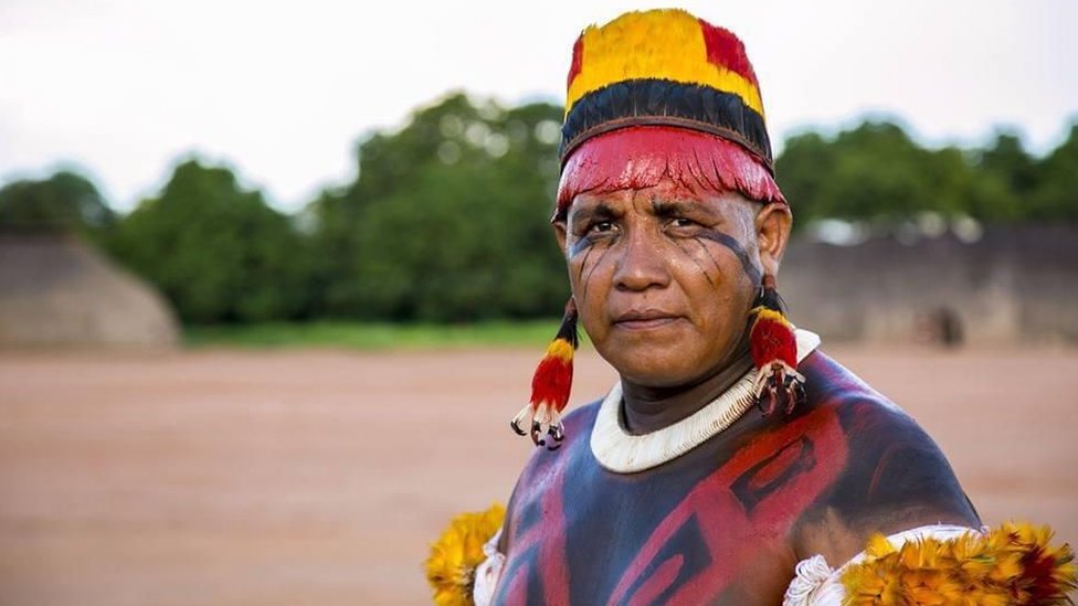 Yanamá Kuikuro, um homem indígena com adereços tradicionais de seu povo, ao ar livre