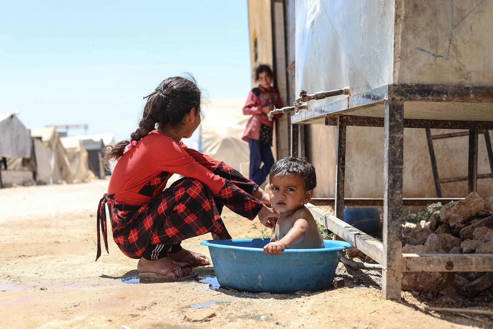 A child sits in a washbowl filled with water next to girls amid extreme heat at the refugee camp, in Idlib, Syria - 13 July 2023