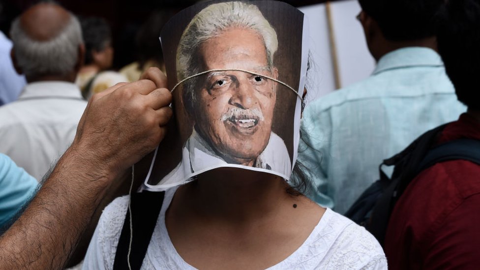 Протестующий поправляет портрет поэта Варавара Рао на лице другого протестующего во время демонстрации против арестов активистов за гражданские и демократические права полицией Махараштры на Парламент-стрит 30 августа 2018 года в Нью-Дели, Индия