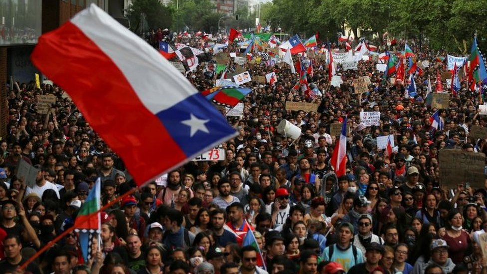 Демонстранты маршируют с флагами и знаками во время акции протеста против государственной экономической модели Чили в Сантьяго, Чили, 25 октября 2019 г.