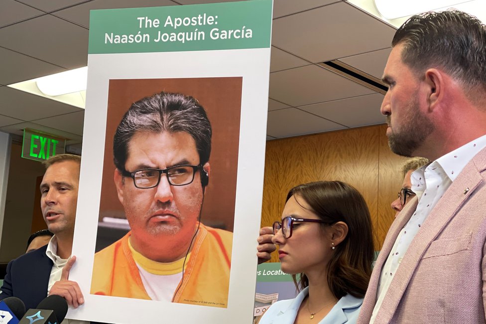 El abogado Mike Rick sostiene un cartel con la cara de Naasón Joaquín García junto a Sochil Martin y Sharim Guzmán.
