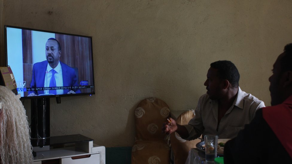 Эфиопы в этом маленьком ресторанчике на севере Эфиопии пристально смотрят телевизор, демонстрирующий своего нового премьер-министра. Хотя у Абия Ахмеда есть свои критики, он чрезвычайно популярен в Эфиопии и во всем мире благодаря своим стремительным реформам с момента прихода к власти в апреле 2018 года.