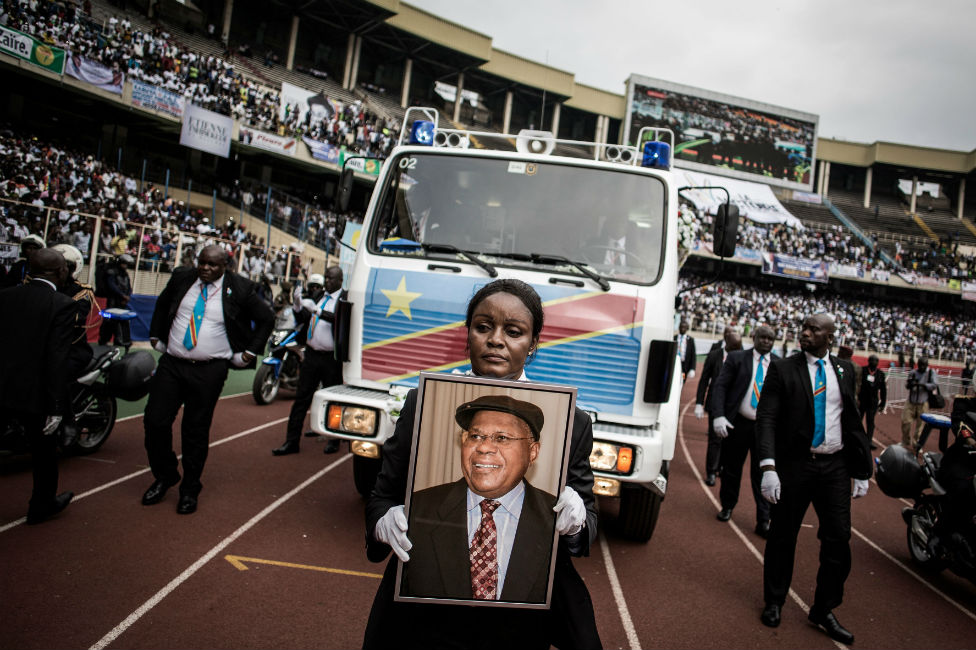 Женщина держит портрет покойного бывшего премьер-министра ДР Конго и лидера оппозиции Этьена Тшисекеди, когда его останки прибывают на траурную церемонию.