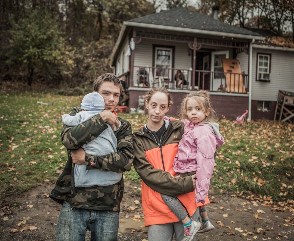 Greg and Ellen holding two children and standing outside a house