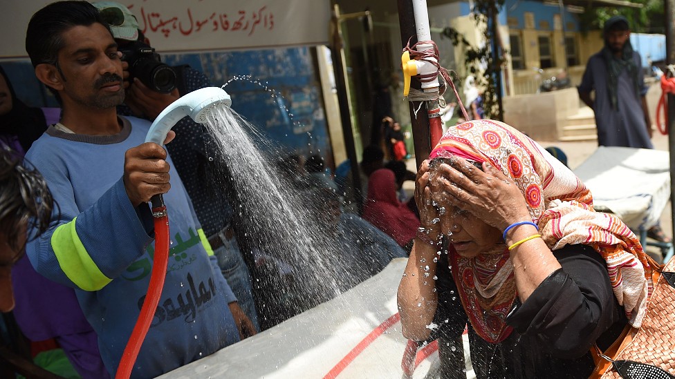 Un hombre moja con agua a una mujer que busca protegerse del calor