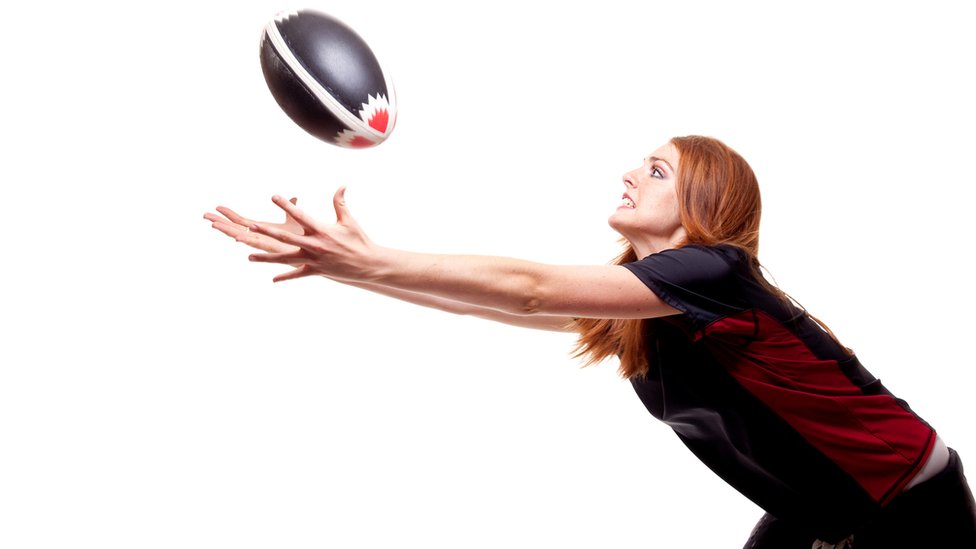 Mujer intentando atrapar una bola de rugby.