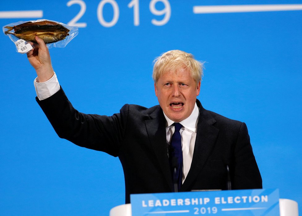 Boris Johnson waves a plastic-wrapped smoked kipper in the air at the final Conservative leadership hustings in London
