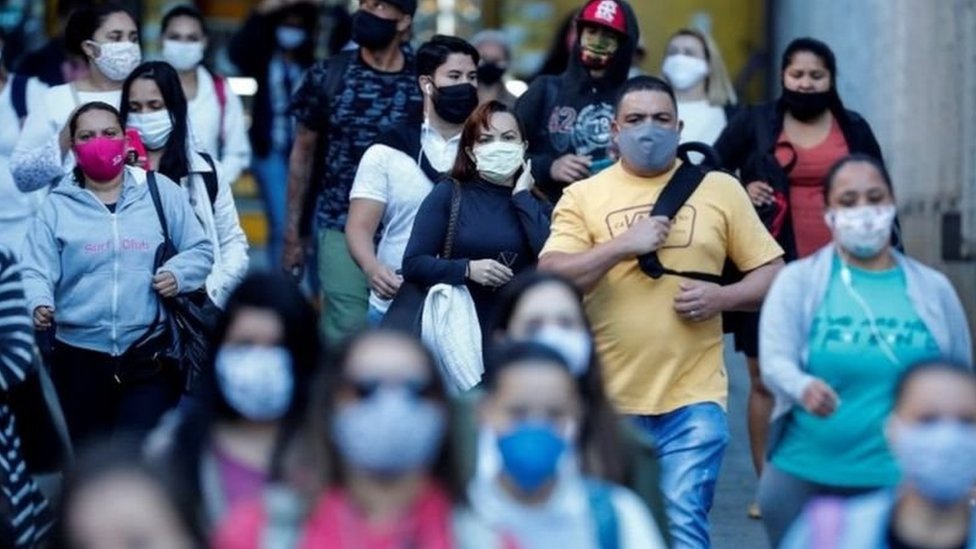 Grande quantidade de pessoas caminha, com máscaras, em cidade brasileira