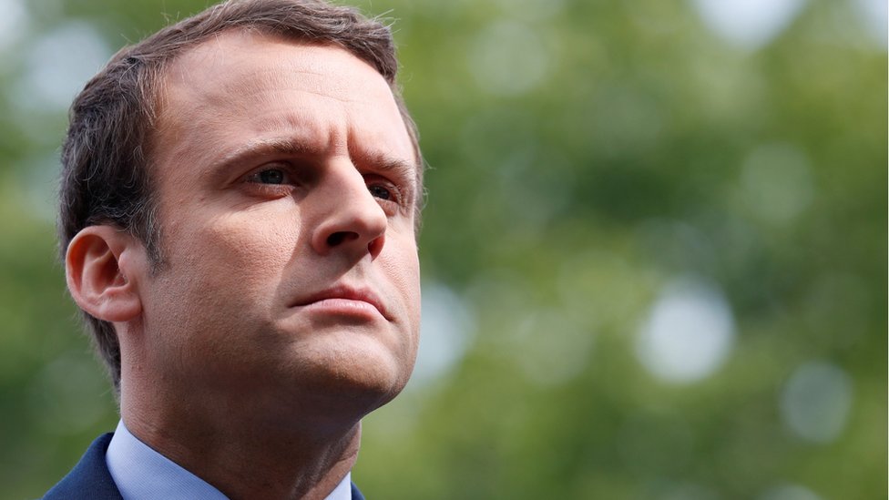 Macron, um homem branco de cabelos castanhos, franze o cenho e olha para cima