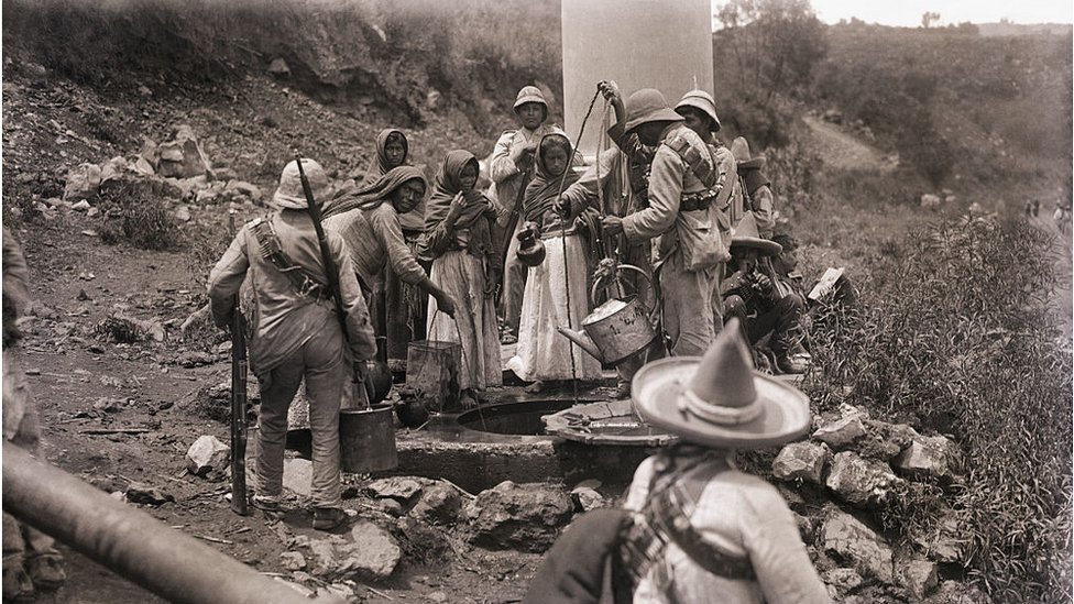 Mujeres y hombres sacan agua de un pozo durante la revolución mexicana.