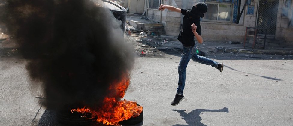 Палестинский демонстрант в маске бросает камень в израильские войска на контрольно-пропускном пункте Каландия, 22 мая