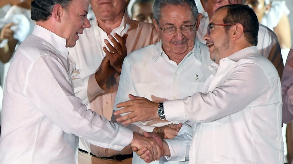 Juan Manuel Santos y y Rodrigo Londoño (comandante de las FARC) se dan la mano en la Habana frente a Raúl Castro.