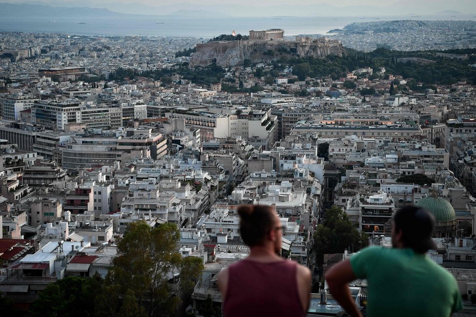 Jóvenes sentados en una colina con el panorama de Atenas enfrente. 8 agosto de 2018