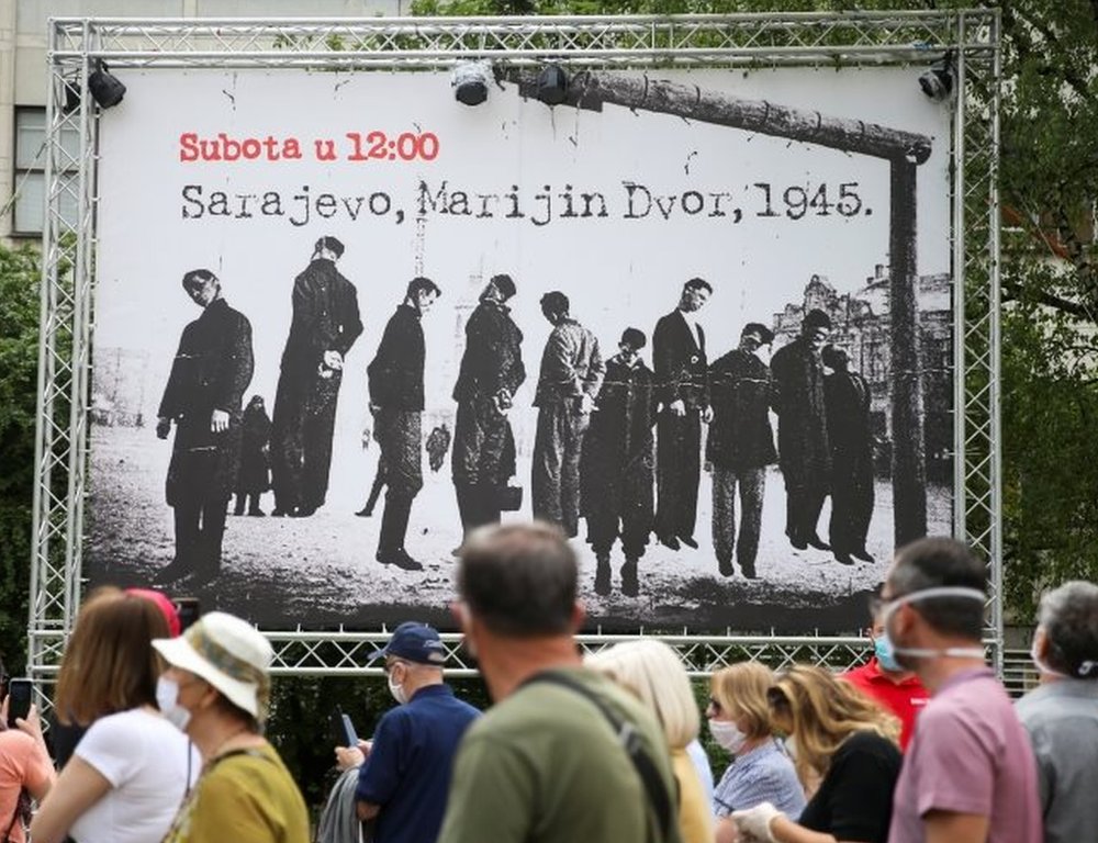 People march past a poster that shows Nazi victims during World War Two
