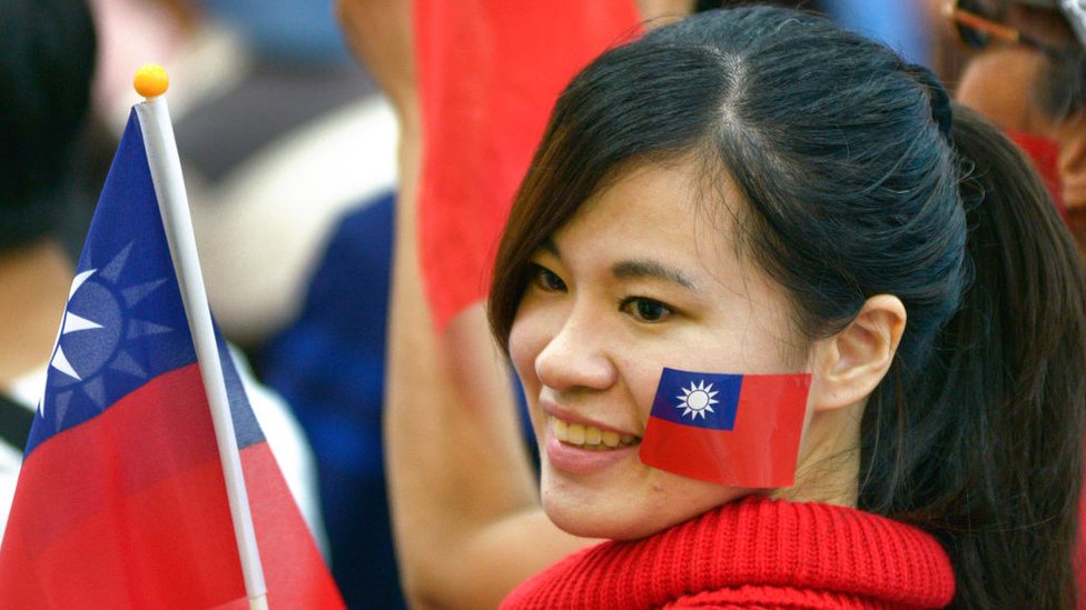 Una joven sonríe mientras sostiene en sus manos una bandera de Taiwán.